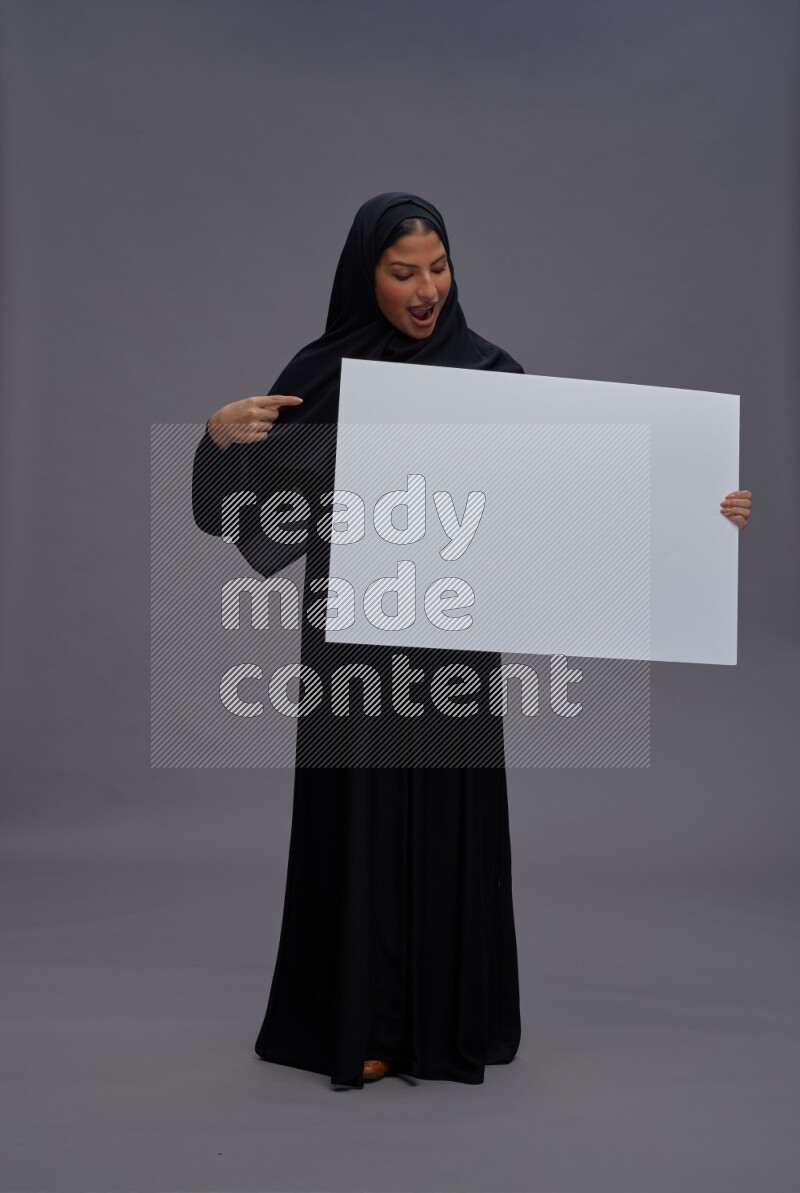 Saudi woman wearing Abaya standing holding white board on gray background