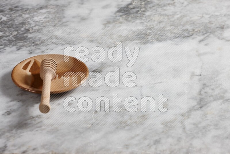 Multicolored pottery plate with wooden honey dipper in it on grey marble background