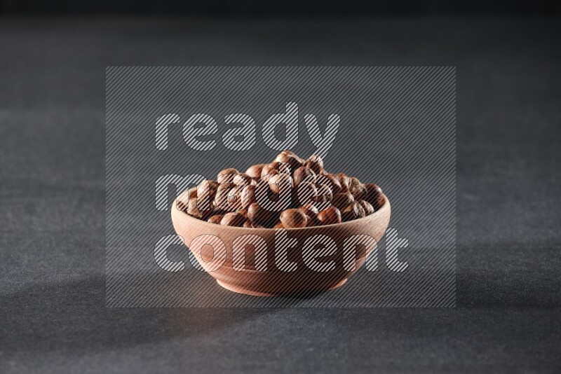 A wooden bowl full of peeled hazelnuts on a black background in different angles