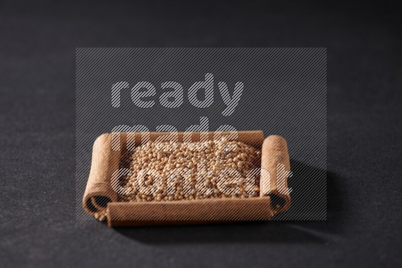 أربعة من أعواد القرفة مكونة شكل مربع بداخلها حبوب الخردل علي خلفية سوداء