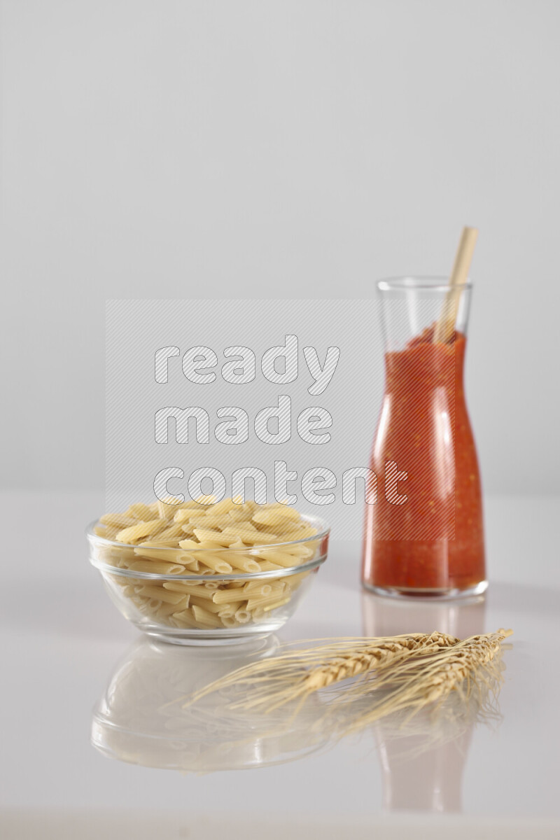 Raw pasta with tomatoe pasta with different ingredients such as cherry tomatoes, basil, garlic, bay laurel, cardamom, white pepper, black pepper, red chilis and wheat stalks on light grey background