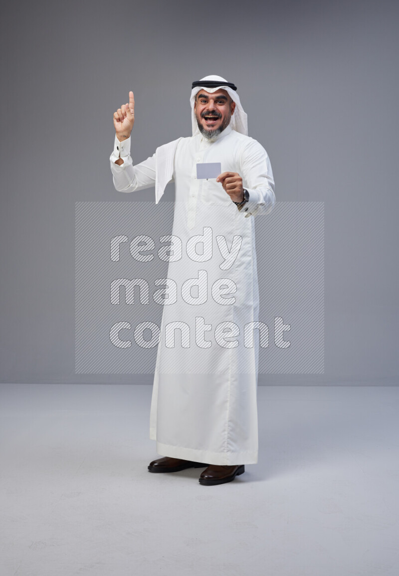 Saudi man Wearing Thob and white Shomag standing holding ATM card on Gray background