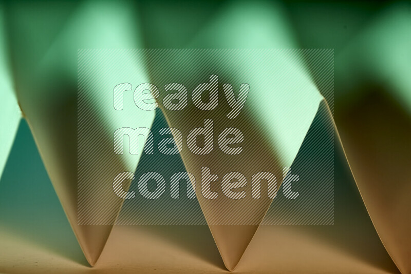 A close-up abstract image showing sharp geometric paper folds in green gradients and warm tones