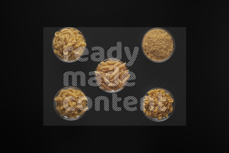 Different pasta types in 5 glass bowls on black background