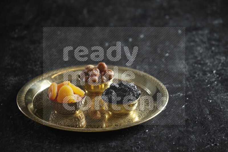 Dried fruits in metal bowls on a tray in a dark setup