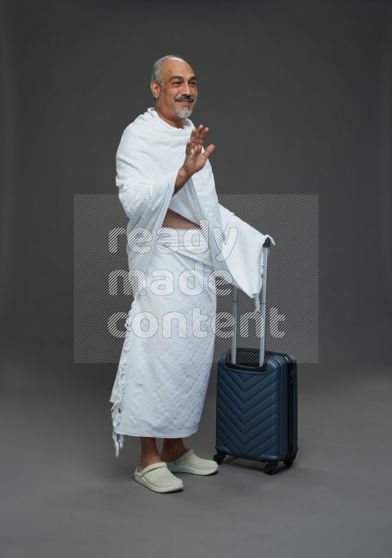 A man wearing Ehram Standing holding traveling bag on gray background