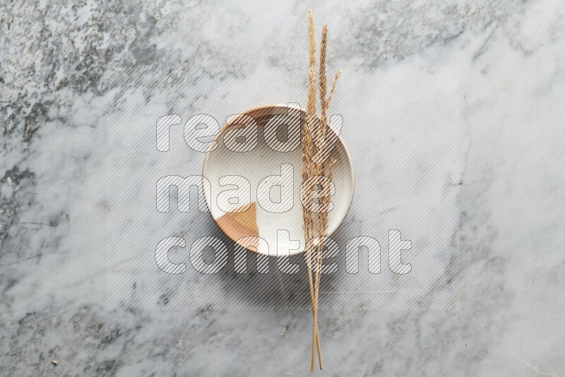 Wheat stalks on multicolored pottery plate on grey marble background