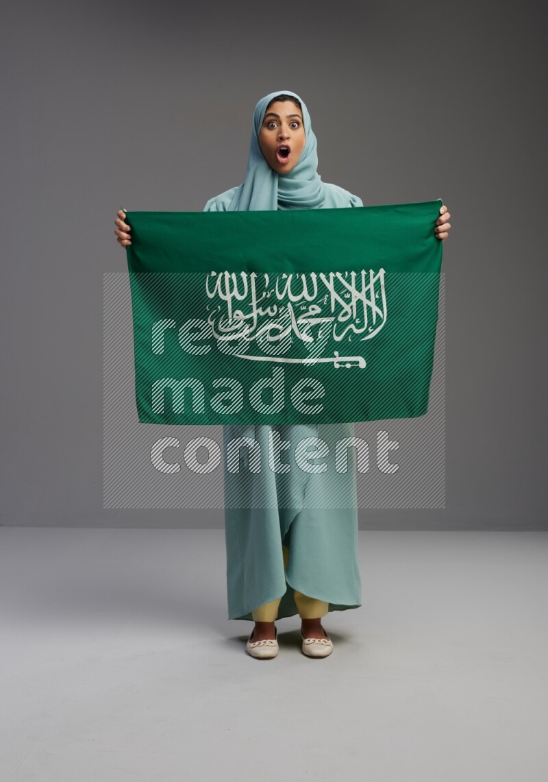 Saudi Woman wearing Abaya standing holding Saudi flag on Gray background