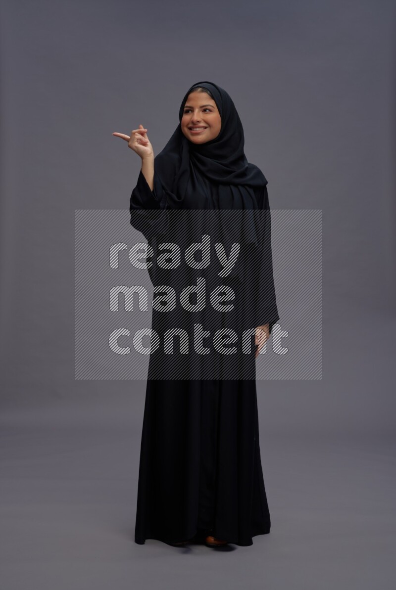 Saudi woman wearing Abaya standing interacting with the camera on gray background
