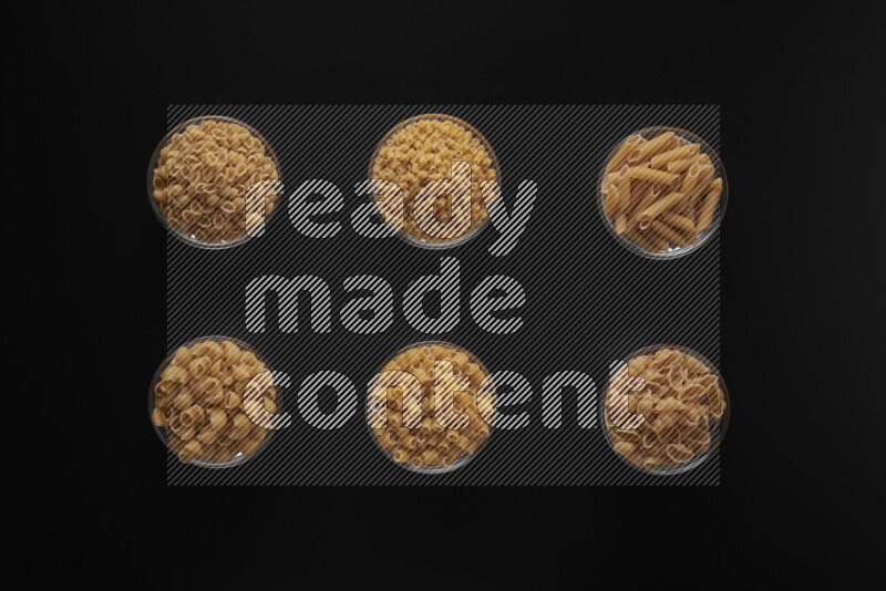 Different pasta types in 6 glass bowls on black background