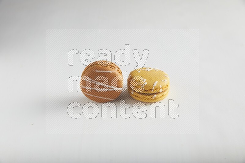 45º Shot of of two assorted Brown Irish Cream, and Yellow Piña Colada macarons on white background