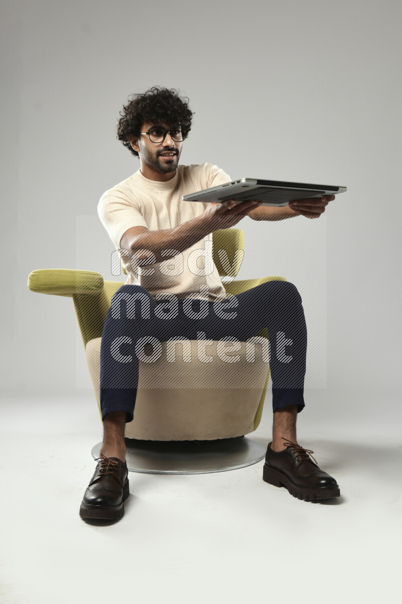 A man wearing casual sitting on a chair holding a laptop on white background