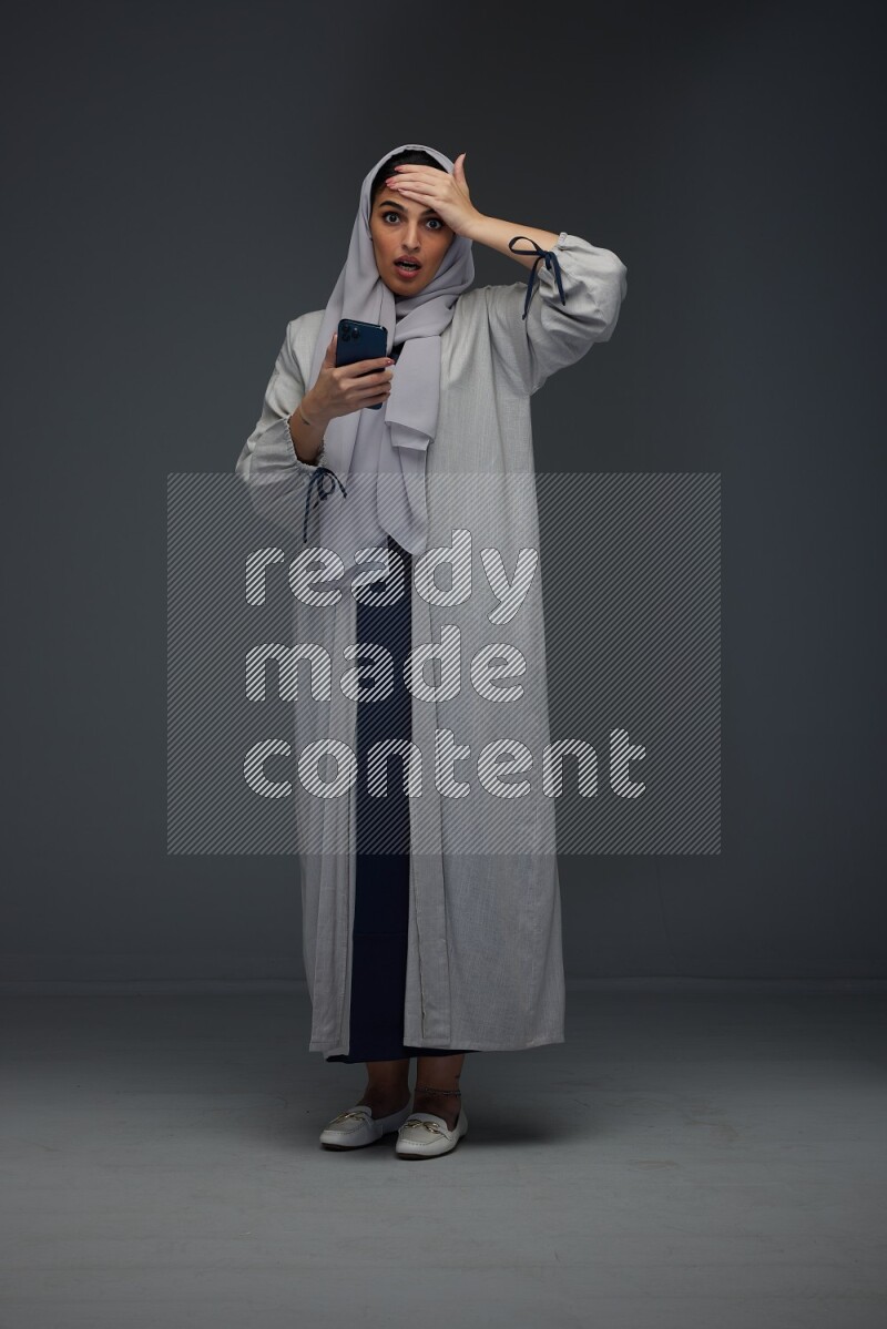 A Saudi woman wearing a light gray Abaya and head scarf standing and pointing in different directions eye level on a grey background