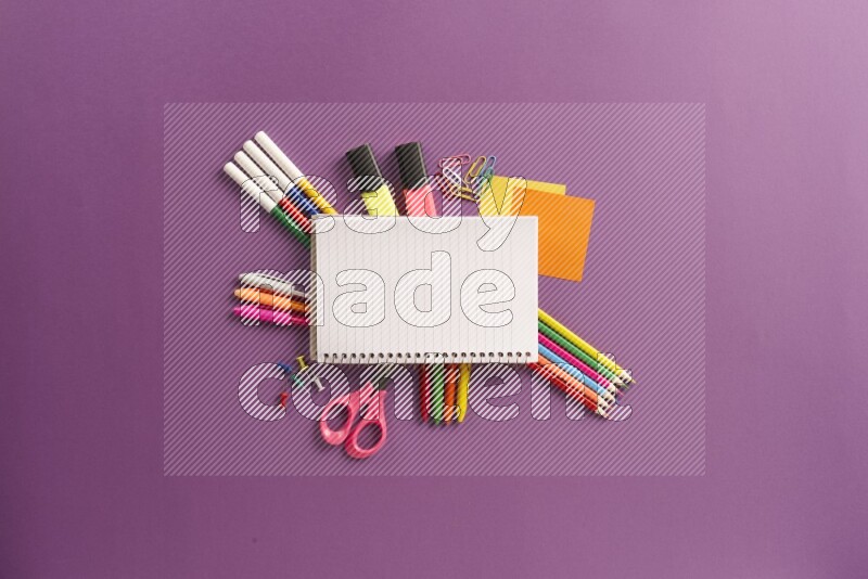A blank open notebook with school supplies on purple background
