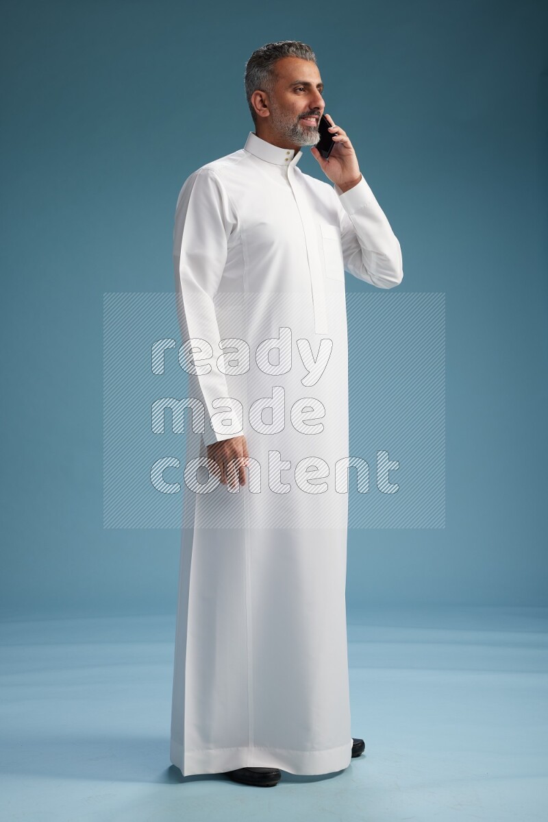 Saudi man wearing thob talking on the phone on blue background