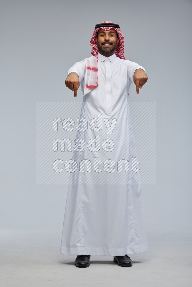 Saudi man Wearing Thob and shomag standing interacting with the camera on Gray background