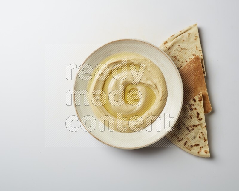 Hummus in a pottry plate garnished with olive oil on a white background