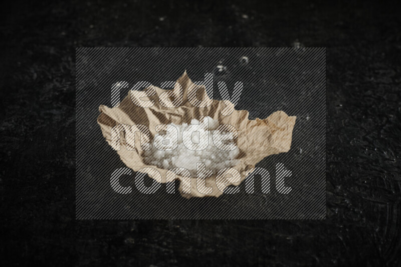 A crumpled piece of paper full of white salt on black background