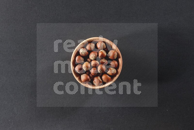 A wooden bowl full of hazelnuts on a black background in different angles