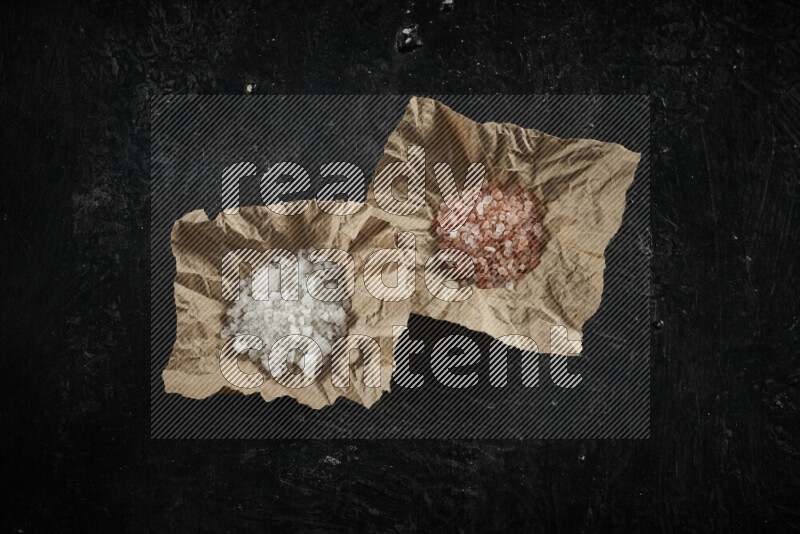 2 crumpled pieces of paper full of pink himalayan salt and white salt on black background