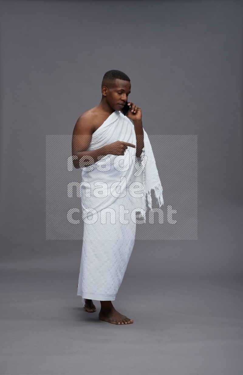 A man wearing Ehram Standing talking on phone on gray background
