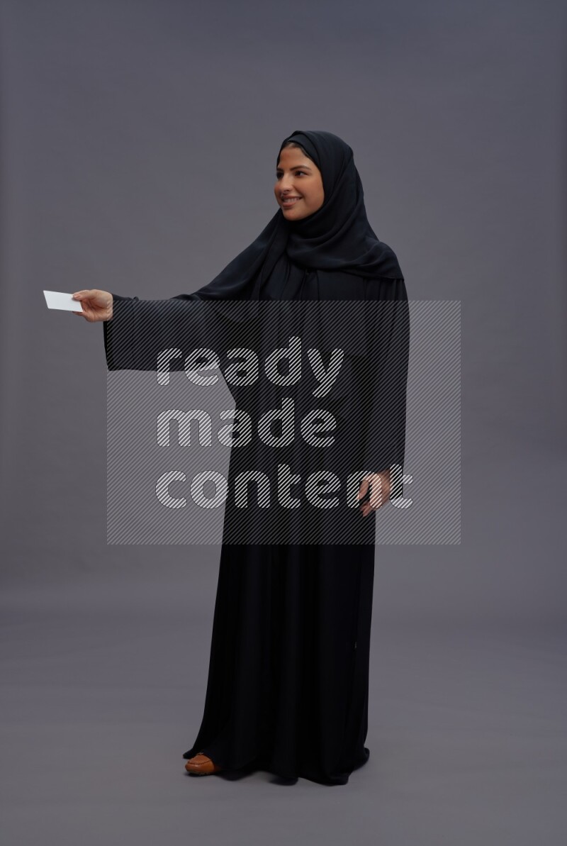 Saudi woman wearing Abaya standing holding ATM card on gray background