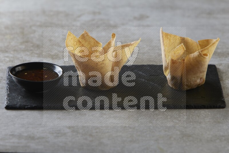 wonton cups with soy sauce ramkin on rectangle slate on grey textured counter top