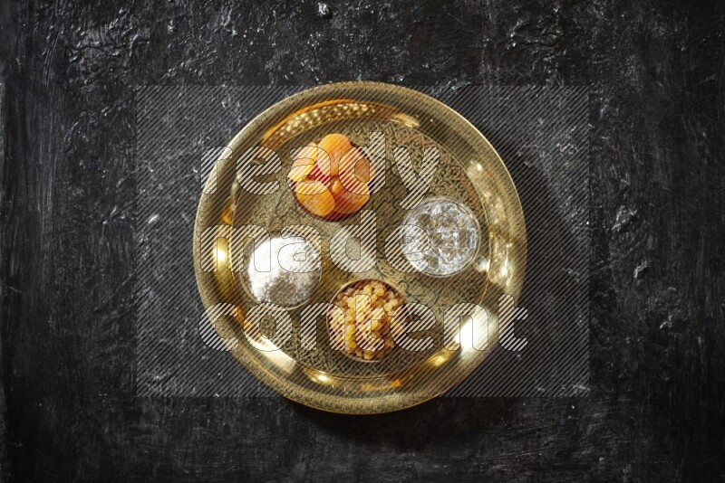 Dried fruits in metal bowls with water on a tray in dark setup