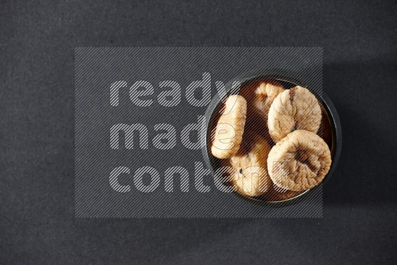 A black pottery bowl full of dried figs on a black background in different angles