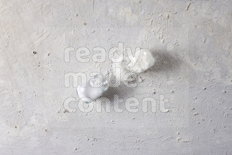 2 glass jars one is filled with table salt and the other with coarse sea salt on white background