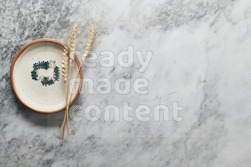 Wheat stalks on decorative pottery plate on grey marble background