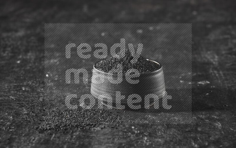 A black pottery bowl full of black seeds on a textured black flooring
