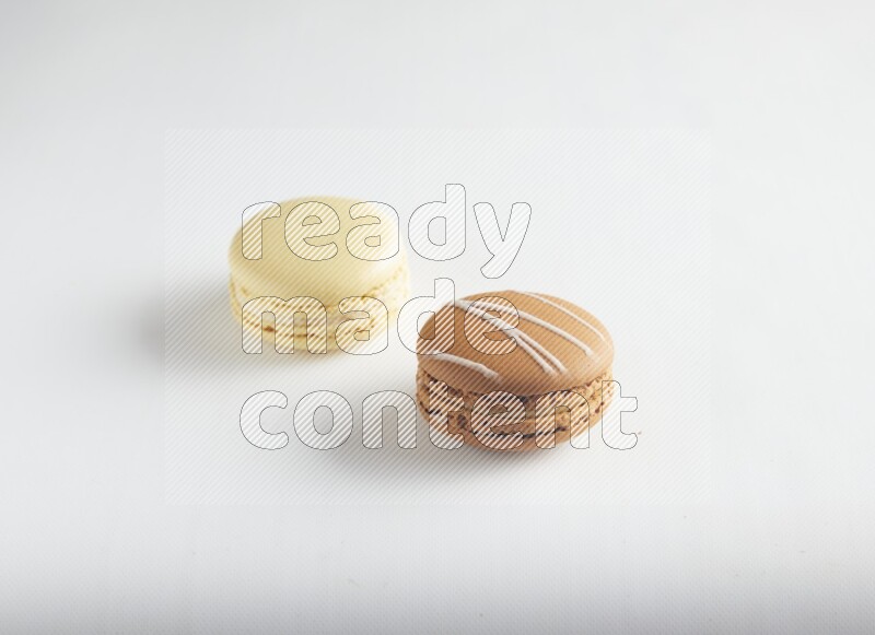 45º Shot of of two assorted Brown Irish Cream, and Yellow Vanilla macarons on white background