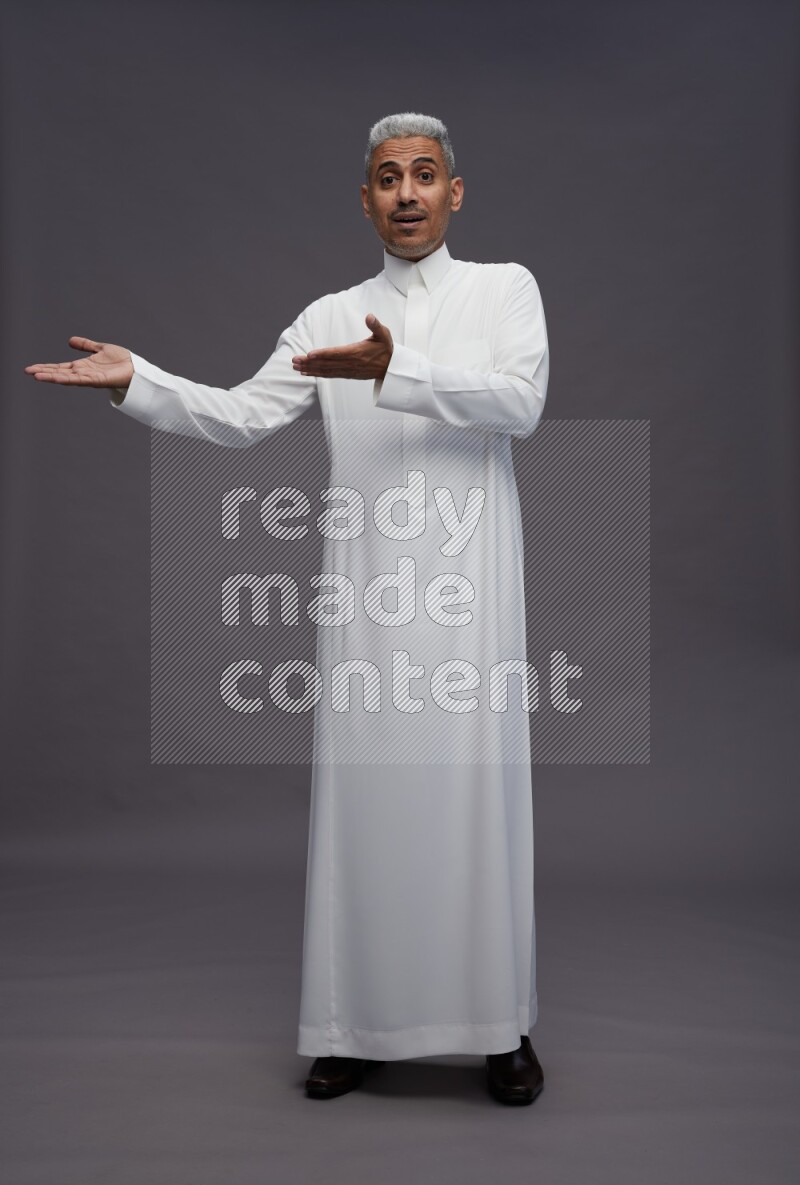 Saudi man wearing thob standing interacting with the camera on gray background