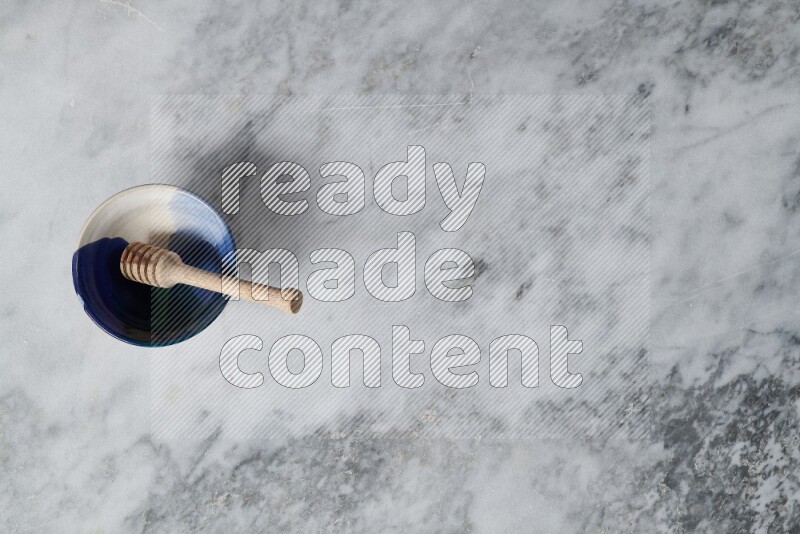 Multicolored pottery bowl with wooden honey dipper in it on grey marble background