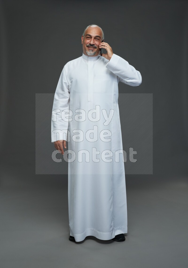 Saudi man without shomag Standing talking on phone on gray background
