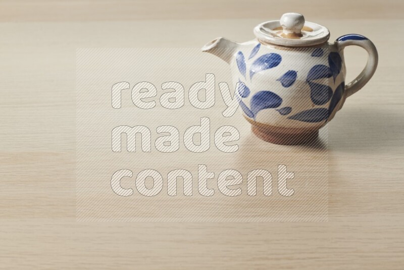 A pottery teapot on light wooden background