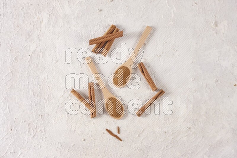 Two wooden spoons full of cinnamon powder with cinnamon sticks on white background