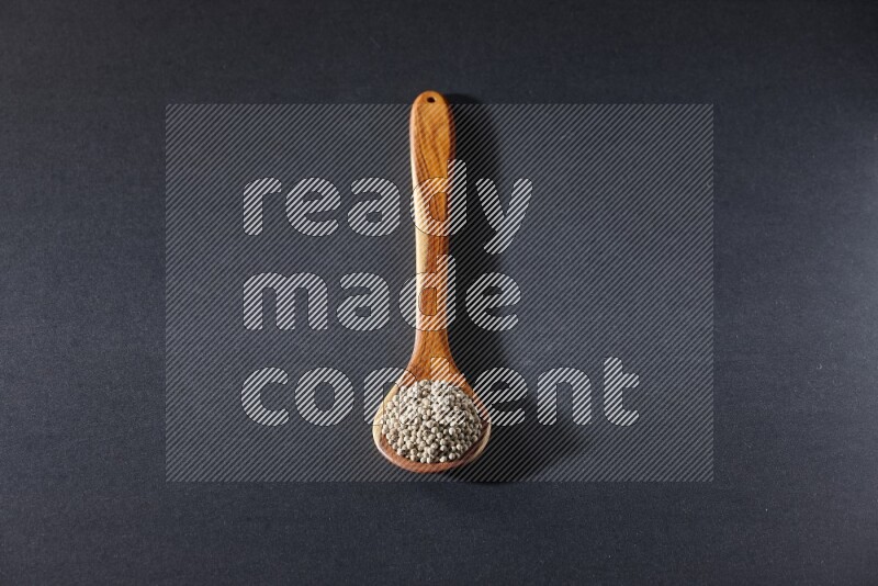 A wooden ladle full of white pepper beads on black flooring