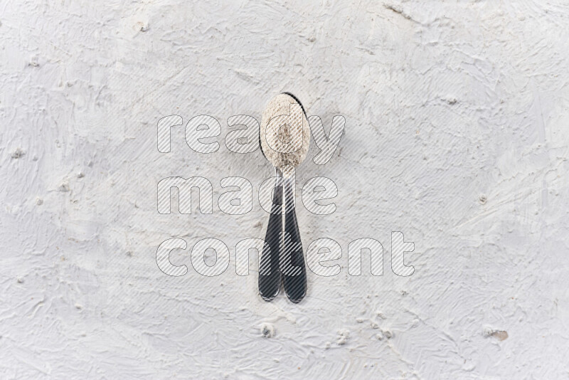 Two metal spoons full of onion powder on white background