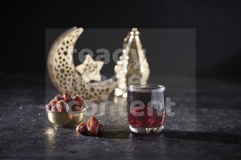 Dates in a metal bowl with Hibiscus beside golden lanterns in a dark setup