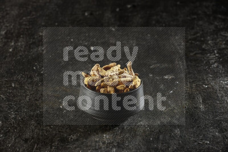 وعاء فخار أسود ممتلئ بأصابع كاملة من الكركم المجفف على خلفية سوداء