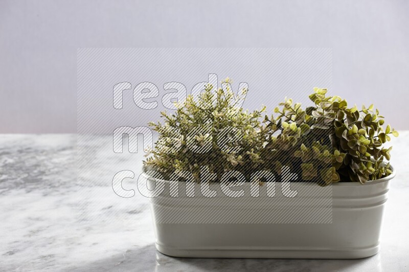 Multiple green artificial plants in white pot on grey marble background