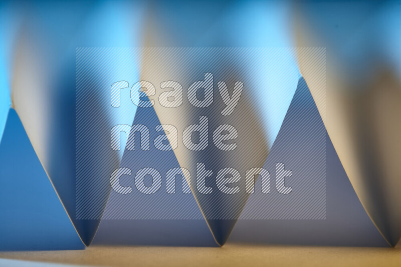 A close-up abstract image showing sharp geometric paper folds in blue gradients and warm tones