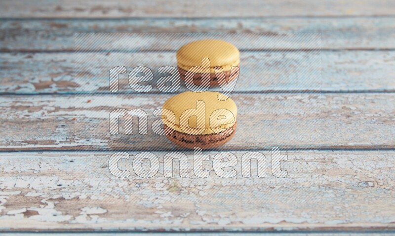 45º Shot of two Yellow and Brown Chai Latte macarons on light blue wooden background