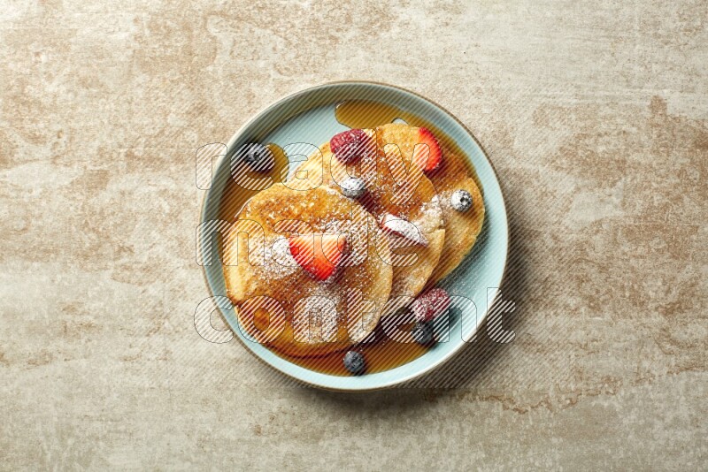 Three stacked mixed berries pancakes in a blue plate on beige background