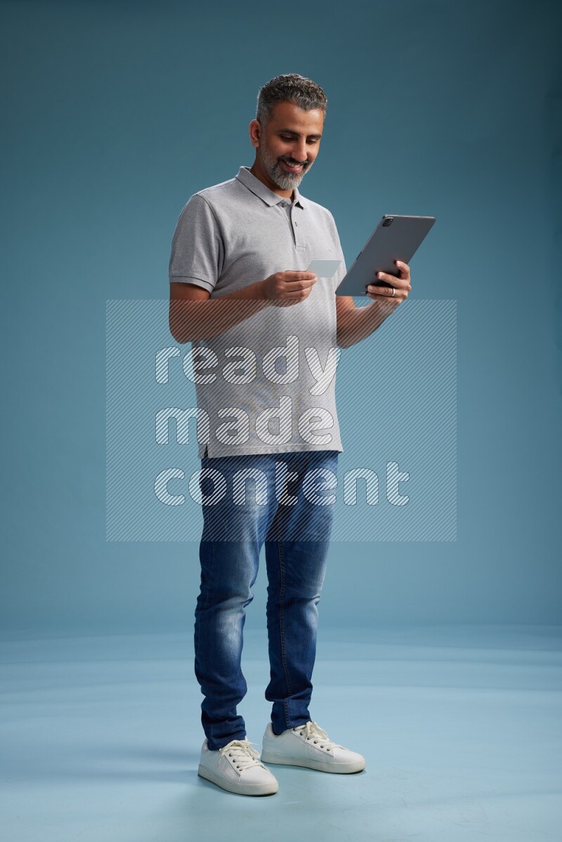 Man Standing holding ATM while working on tablet on blue background