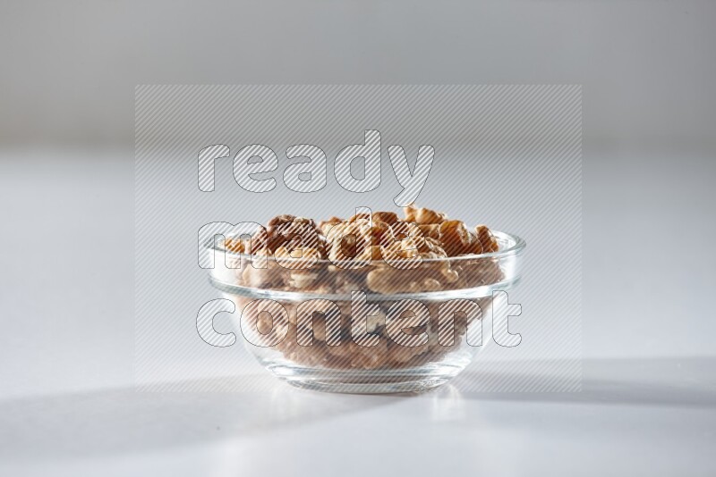 A glass bowl full of peeled walnuts on a white background in different angles