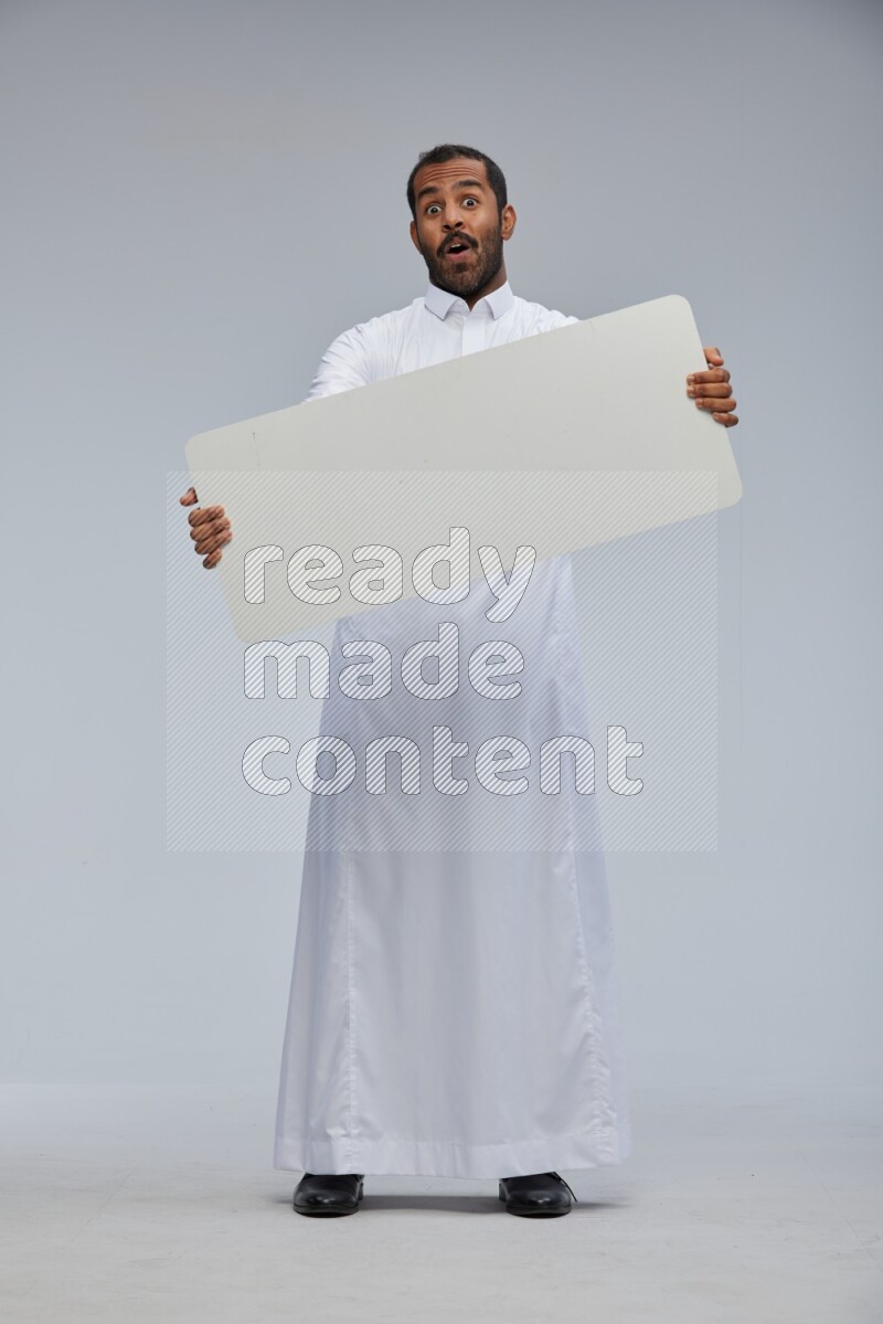Saudi man wearing Thob standing holding board on Gray background
