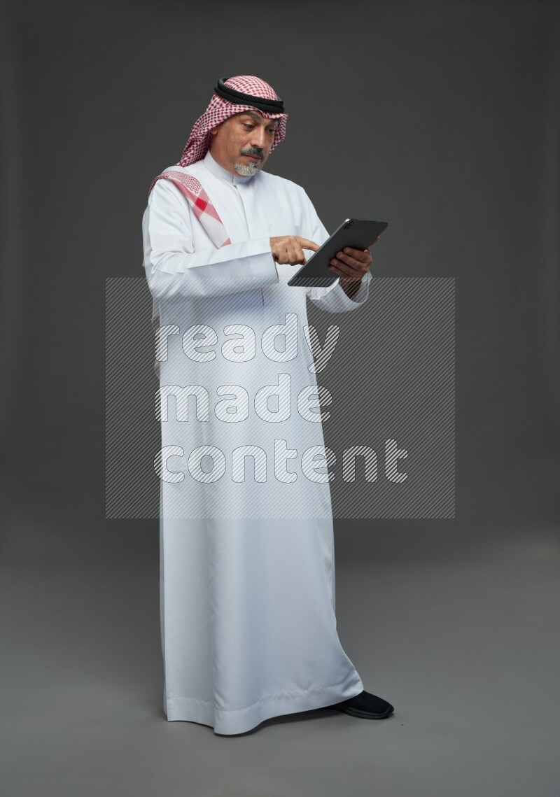 Saudi man with shomag Standing working on tablet on gray background
